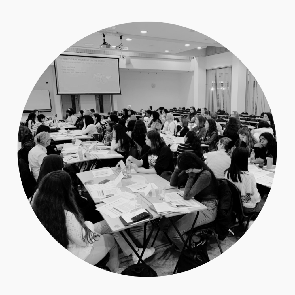 A black and white workshop of about 80 people sitting at tables in working groups